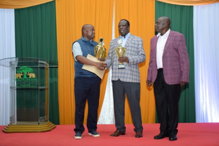 A representative of the Sacco is awarded trophies by CS Wycliffe Oparanya and CAK CEO Daniel Marube. Co-op News Ngarisha Sacco